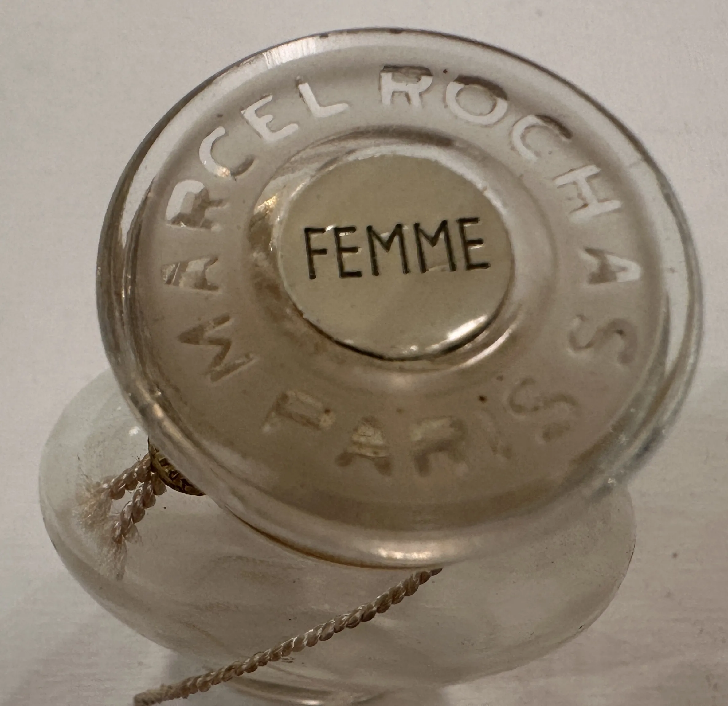 Flacon de parfum antique de Marcel Rochas de couleur claire avec le mot Femme inscrit au bas.