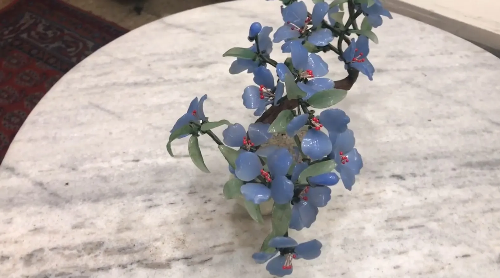 Bonsai antico con fiori blu su tavolo di marmo.