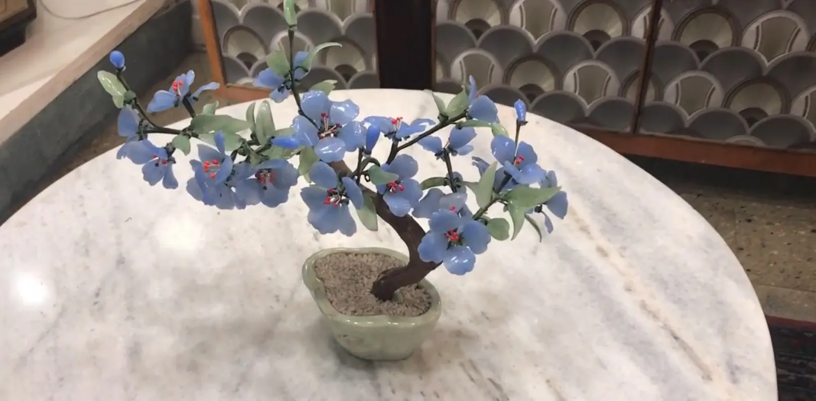 Antiker Bonsai mit blauen Blumen auf einem Marmortisch.