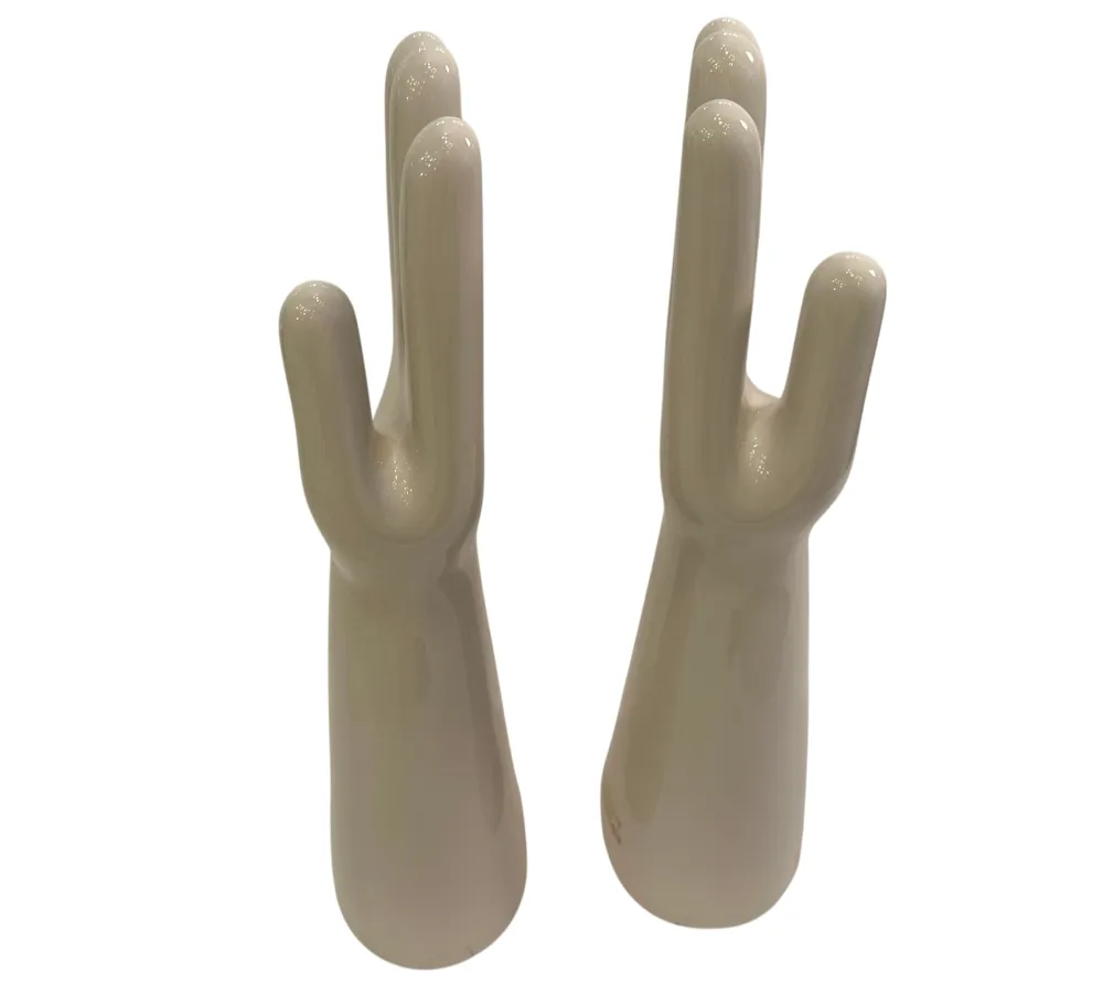 Coppia di mani in ceramica, antiche e lucide, con dettagli nella forma in uno sfondo neutro.