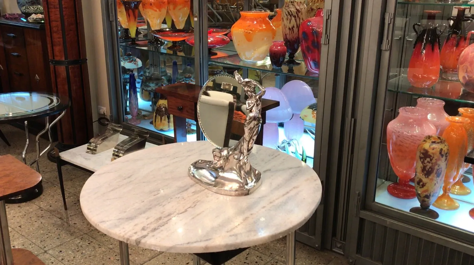 Miroir ancien avec base en statue, décoration stylisée, fond avec des vases colorés.