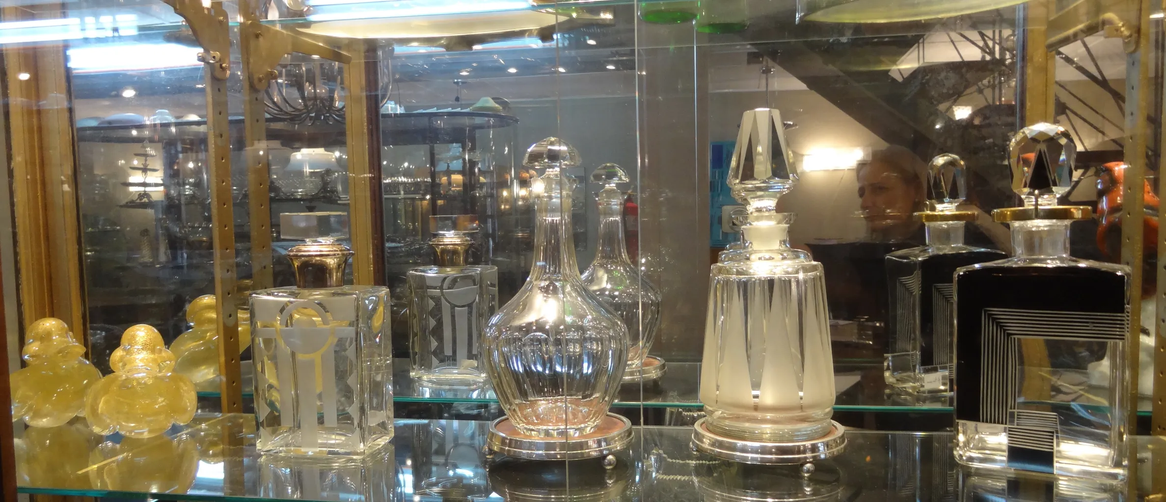 Garrafa antiga com design elegante e detalhes decorativos, em uma vitrine com outras antiguidades.