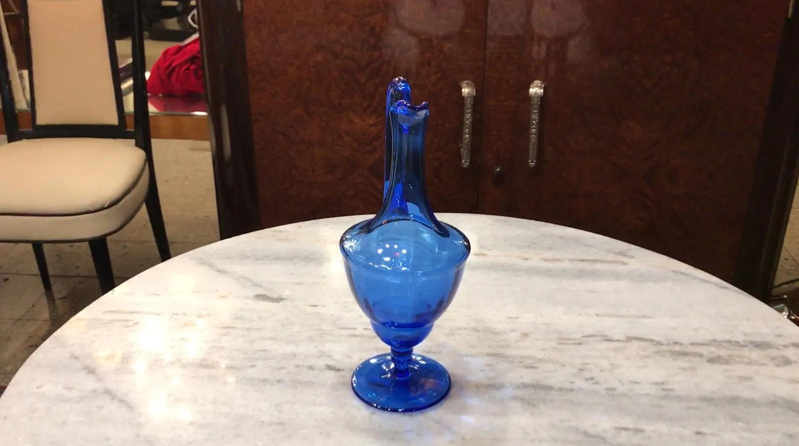 jarra antigua de cristal azul sobre mármol, con fondo de muebles
