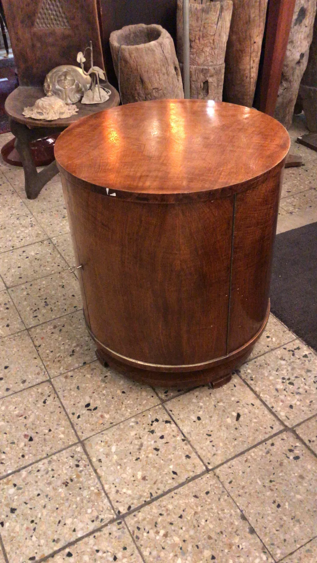 Mobile bar antico con superficie rotonda, circondato da oggetti decorativi.