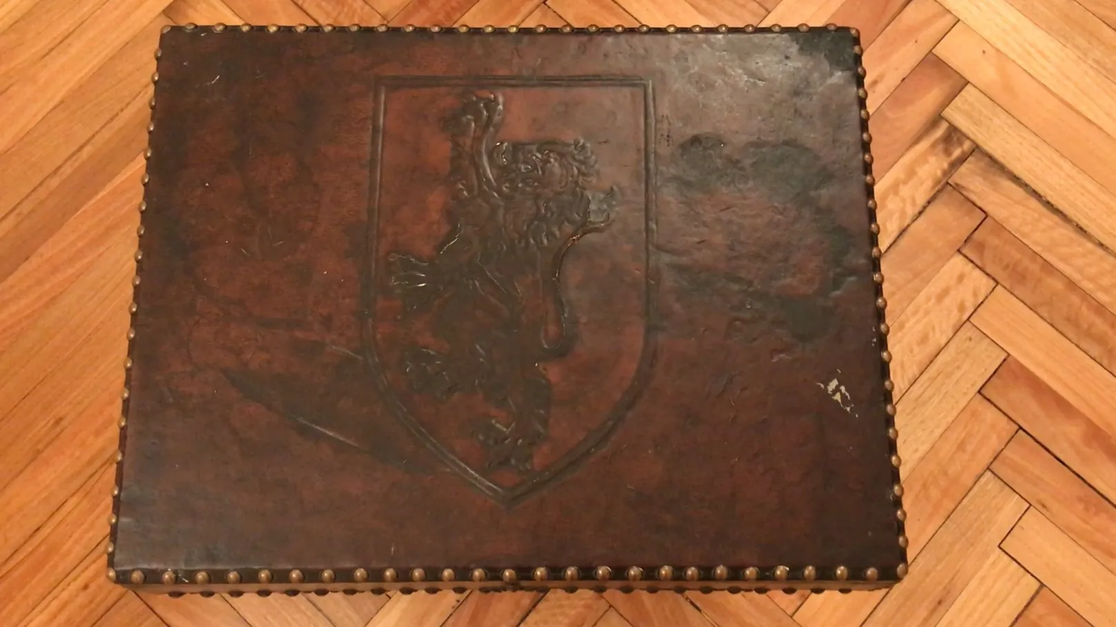 Mueble bar antiguo de madera con un león tallado y clavos decorativos.