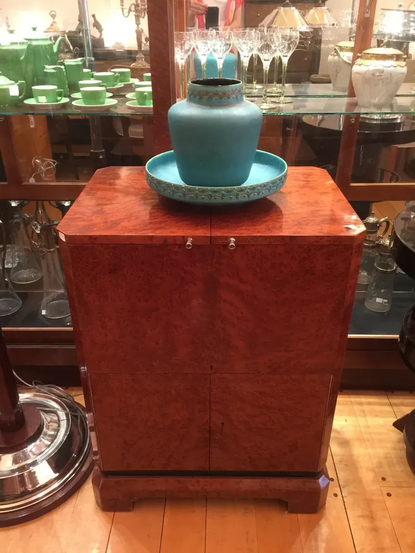 Mueble bar antiguo con decoraciones elegantes y un jarrón azul.