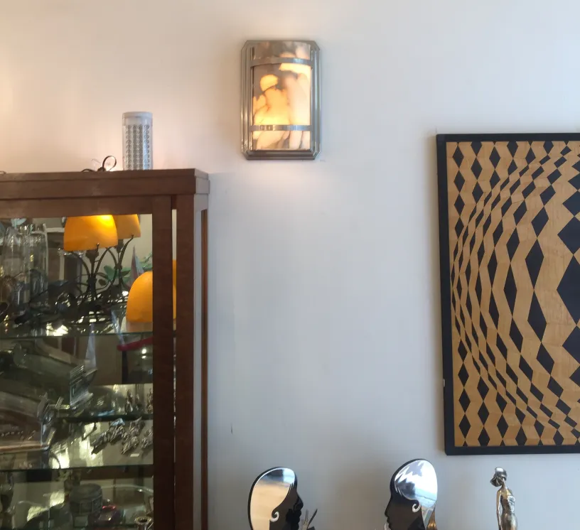 Pair of antique sconces on wall, featuring elegant design, illuminating a cozy ambiance with a cabinet nearby.