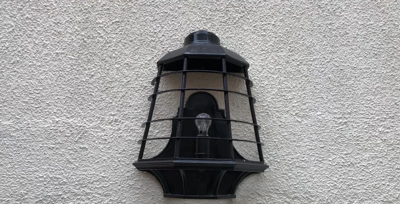 Coppia di applique antiche nere con griglia e lampadina su muro bianco