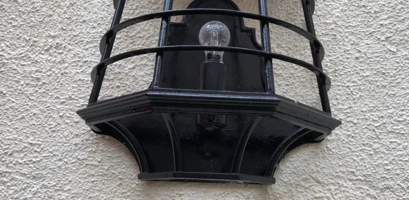 Antiker schwarzer Wandleuchter mit sichtbarem Glühbirnen, hellem Hintergrund.