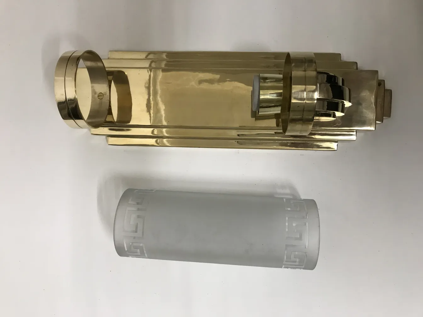 Par de apliques antiguos con elegante diseño geométrico, uno brilla en acabado dorado y el otro tiene un difusor de vidrio. Ambiente iluminado y acogedor.