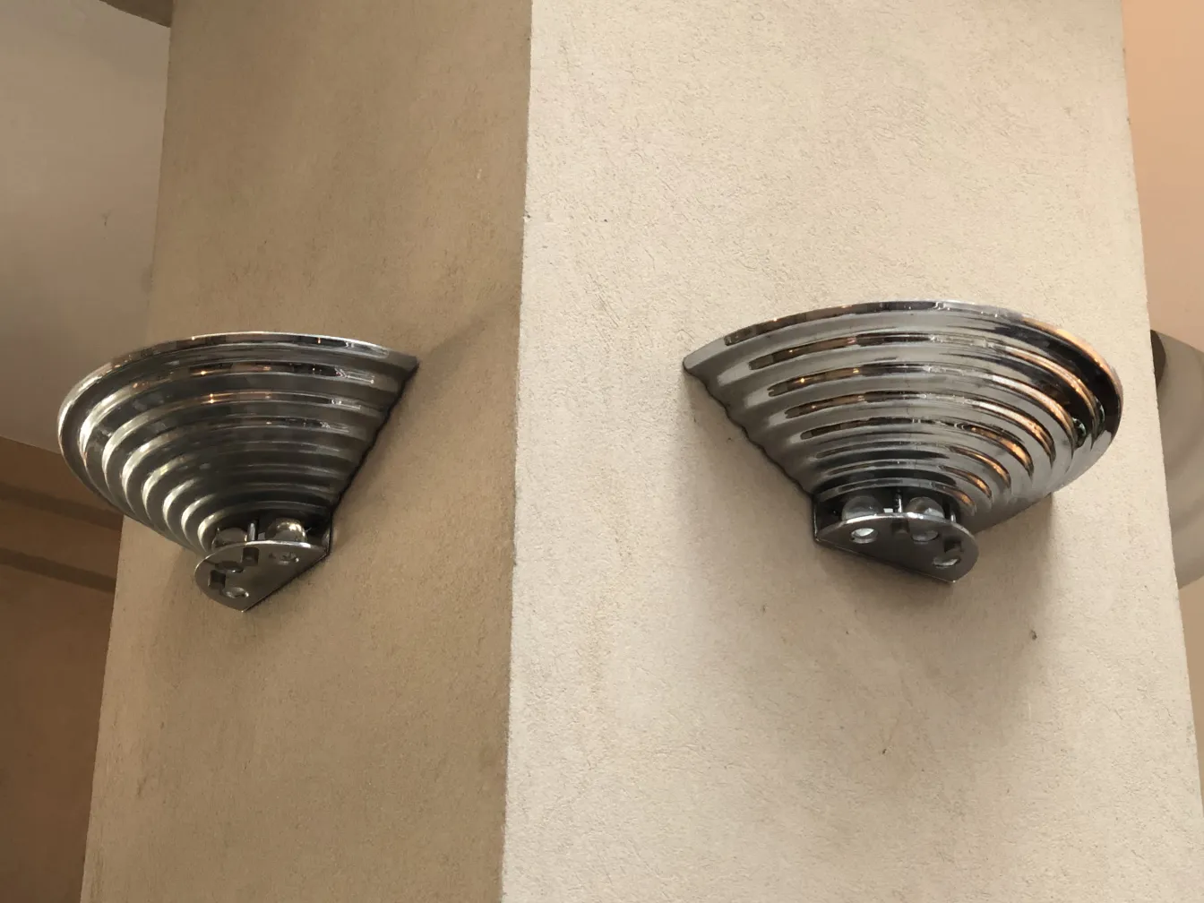 Par de luminárias de parede antigas com design curvo, montadas em uma parede clara.