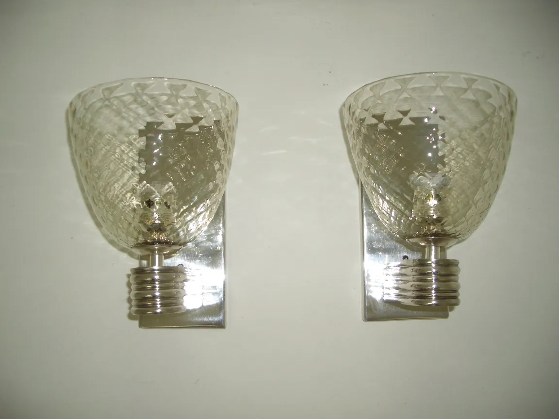 Antigo par de luminárias de parede de vidro com base metálica brilhante, montadas em uma parede branca.