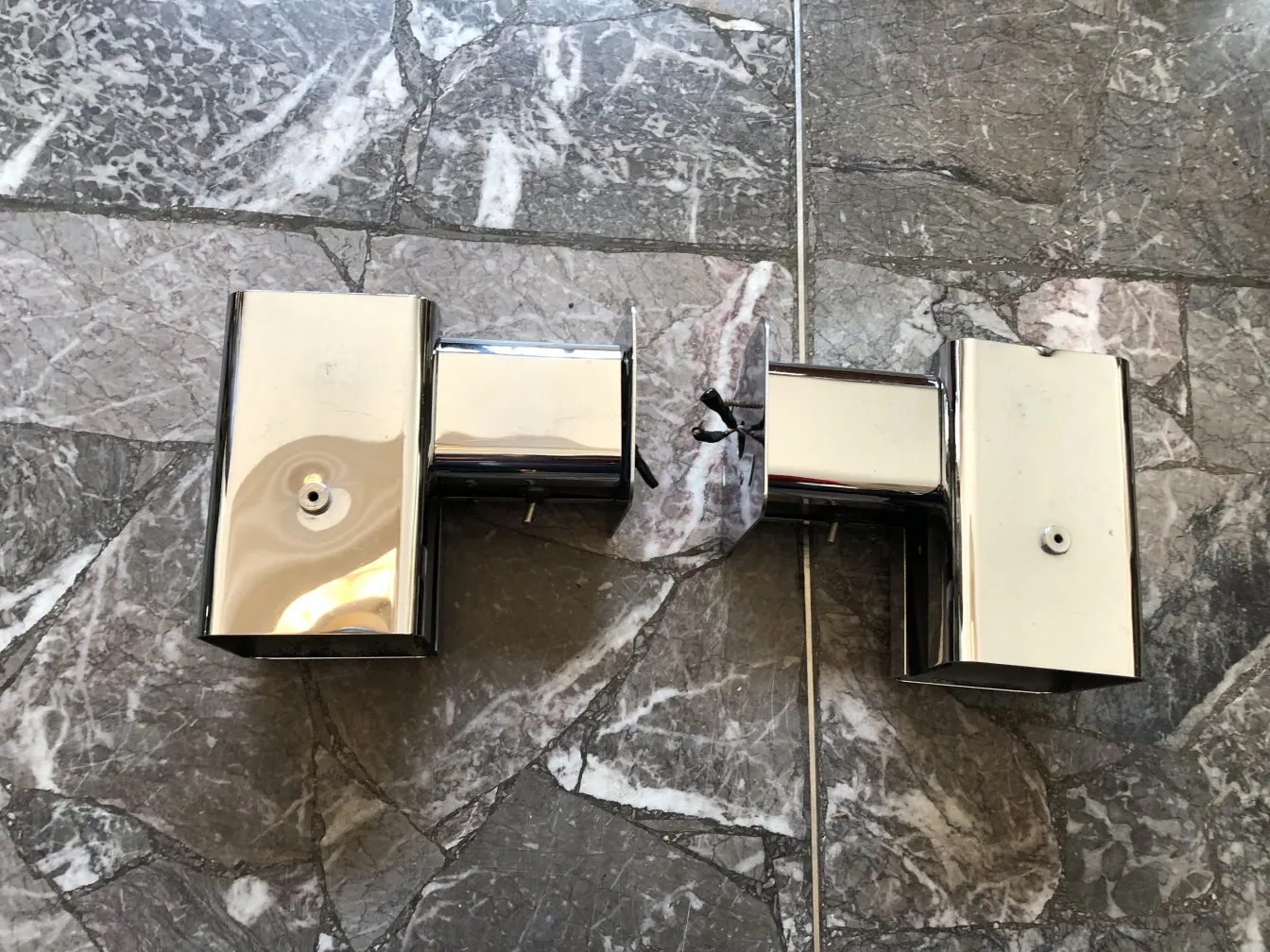 Pair of antique sconces, shiny finish, set against marble backdrop.