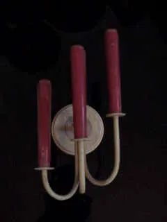 Paire d'appliques anciennes avec des bras courbés et des bougies rouges sur un fond sombre.