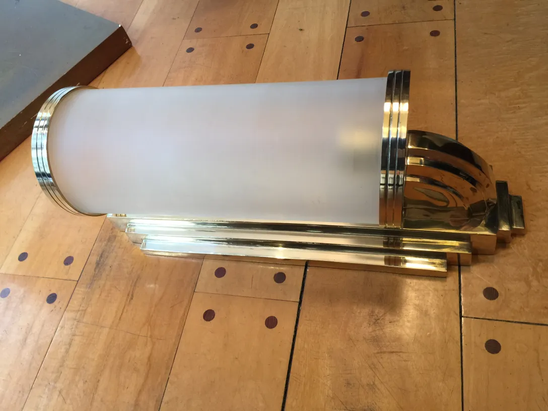 Antica coppia di applique con design classico ed elegante, che illuminano uno spazio in legno chiaro.