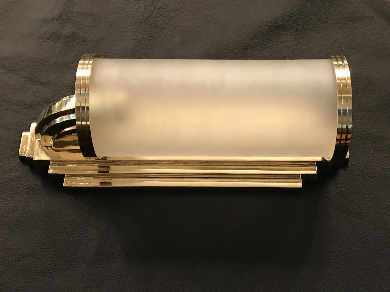 Gold sconces with frosted glass, antique style, against black leather background.