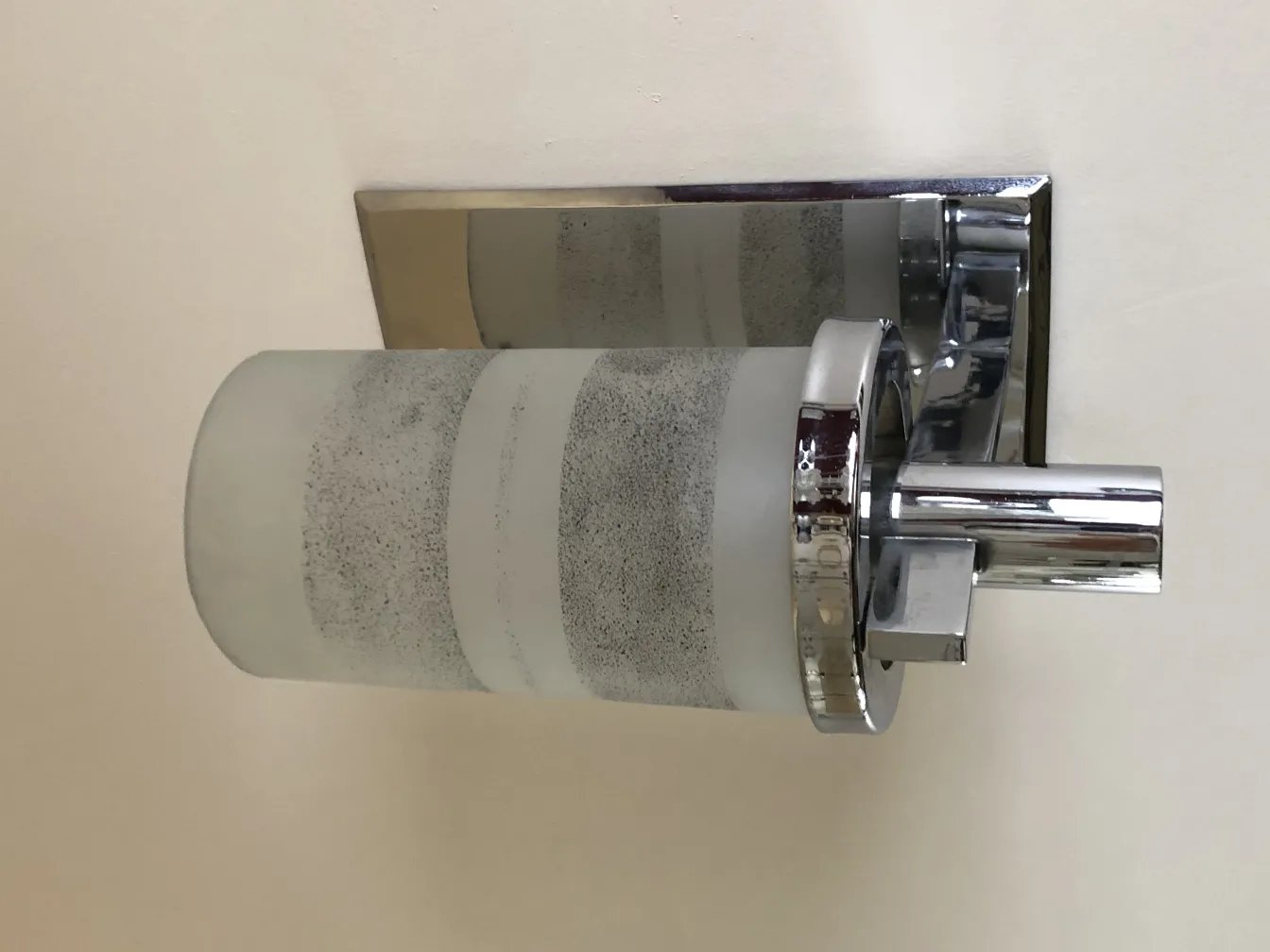 Paar zylindrischer Wandleuchter mit Metallelementen, die eine helle Wand beleuchten.