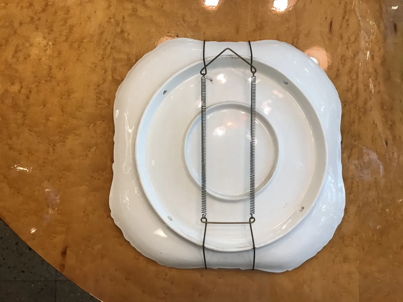 Antica ceramica bianca con supporto in metallo su sfondo marrone.