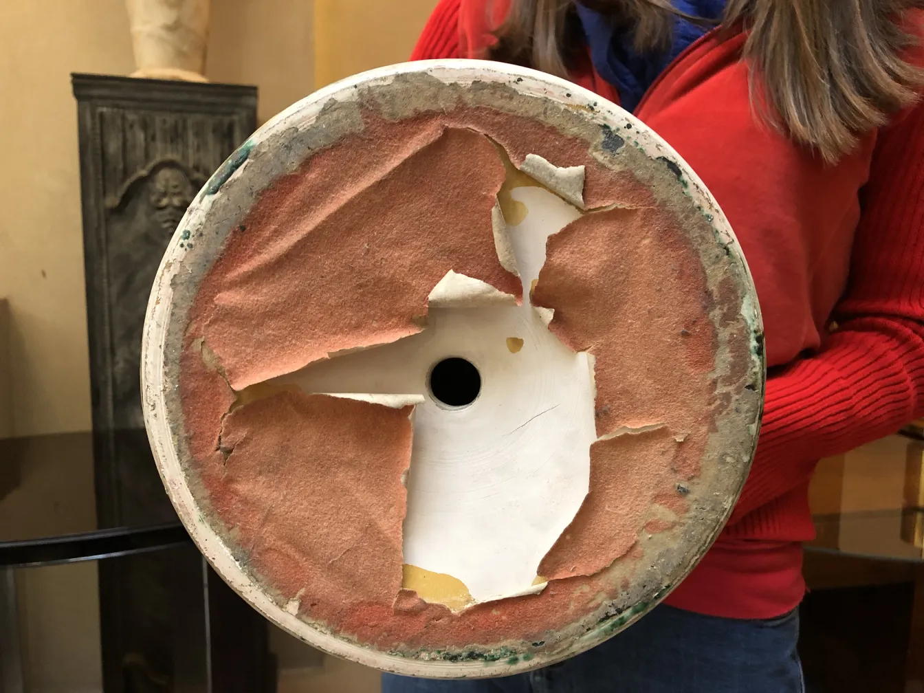 Vista inferiore di una ceramica antica con base danneggiata, circondata da un ambiente accogliente.