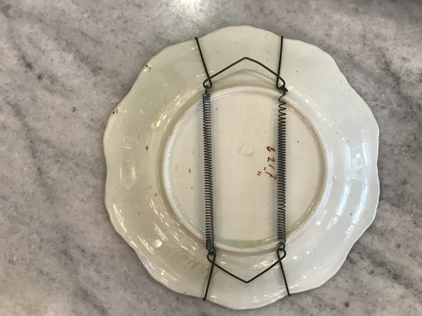 Antico piatto in ceramica bianca con supporto in metallo, visto dal basso.