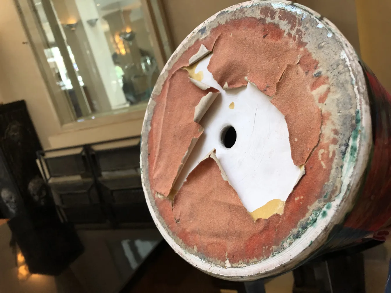 प्राचीन-घी-पात्र का आधार दृश्य, जिसमें रंगीन पैटर्न और घिसी हुई विवरण हैं।