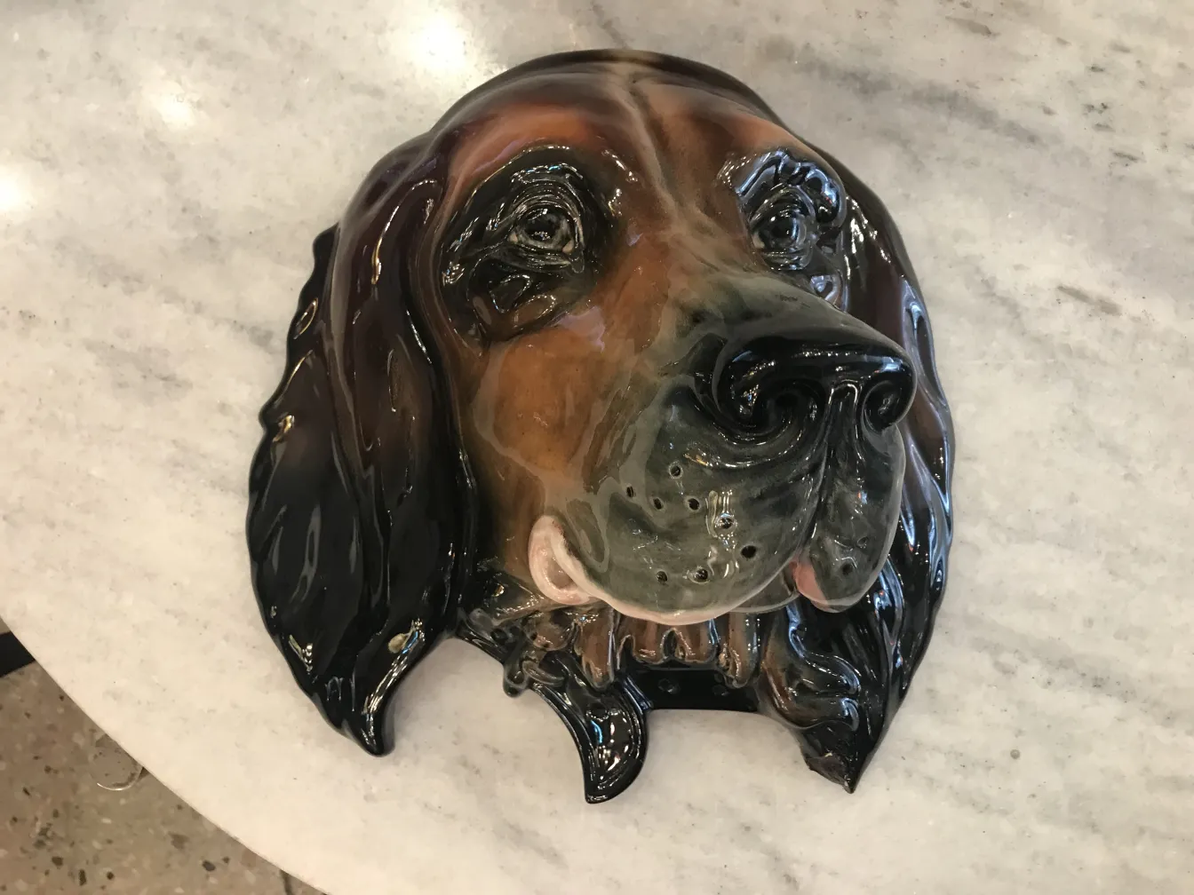 Scultura di ceramica antica a forma di cane, lucida e dettagliata, su una superficie chiara.