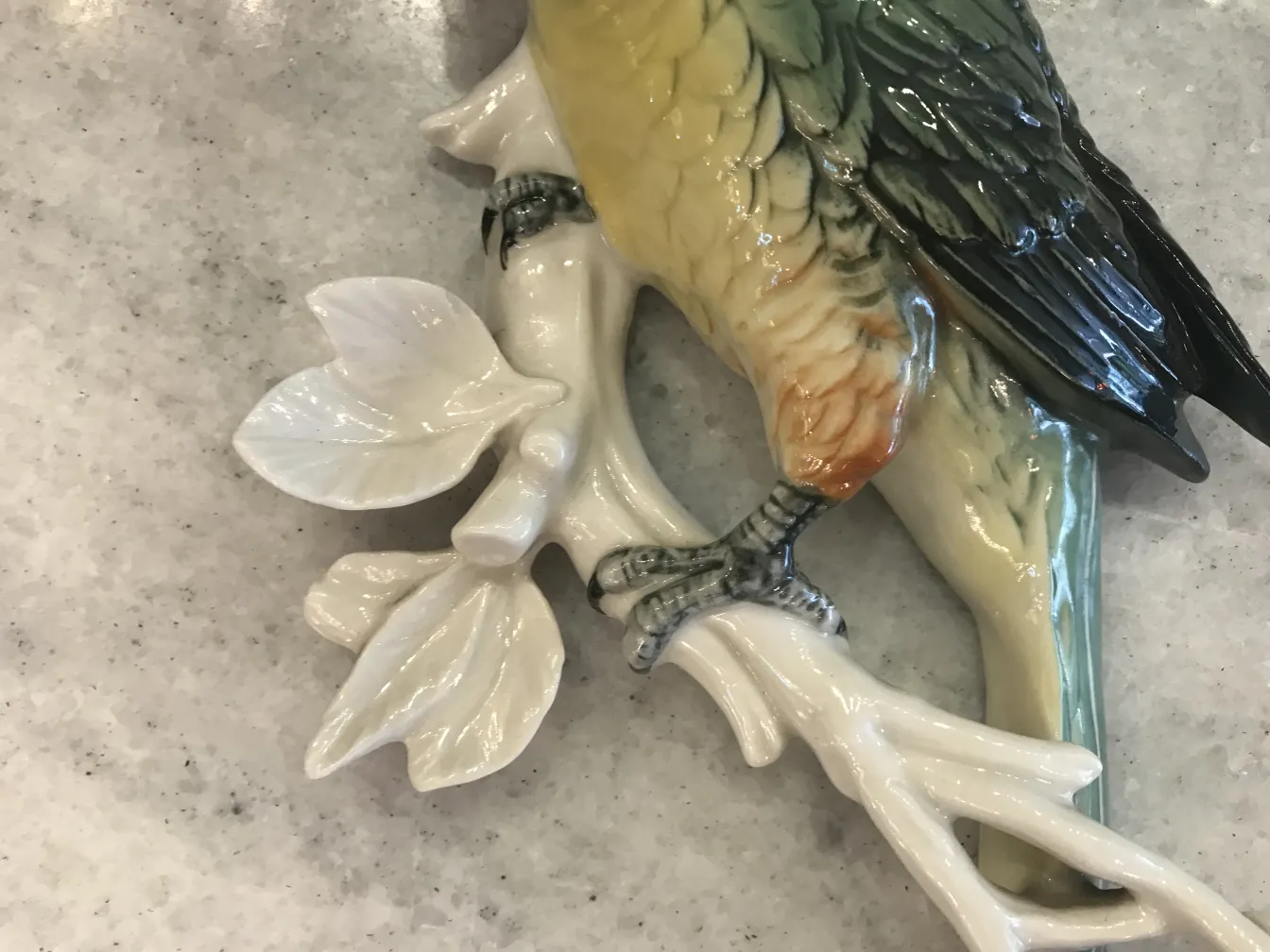 scultura in ceramica antica con un uccello colorato su rami