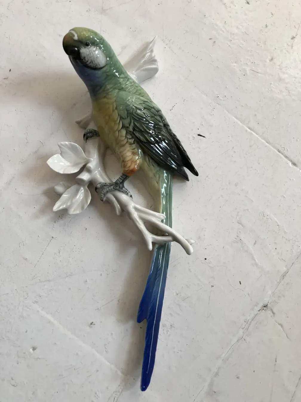 Antica figura di ceramica di un uccello colorato su un ramo bianco.