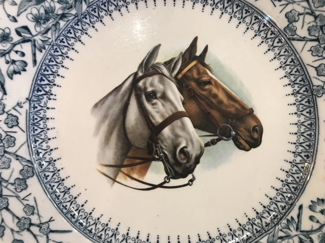 Plato de cerámica antigua con imagen de caballos grises y marrones, decorado con flores azules.