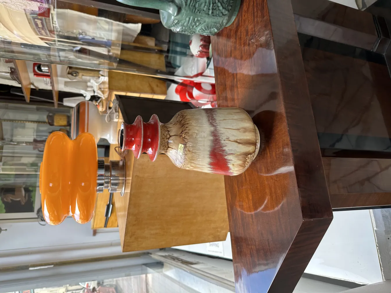 Vaso de cerâmica antiga com detalhes em vermelho e marrom, cercado por outros itens decorativos.