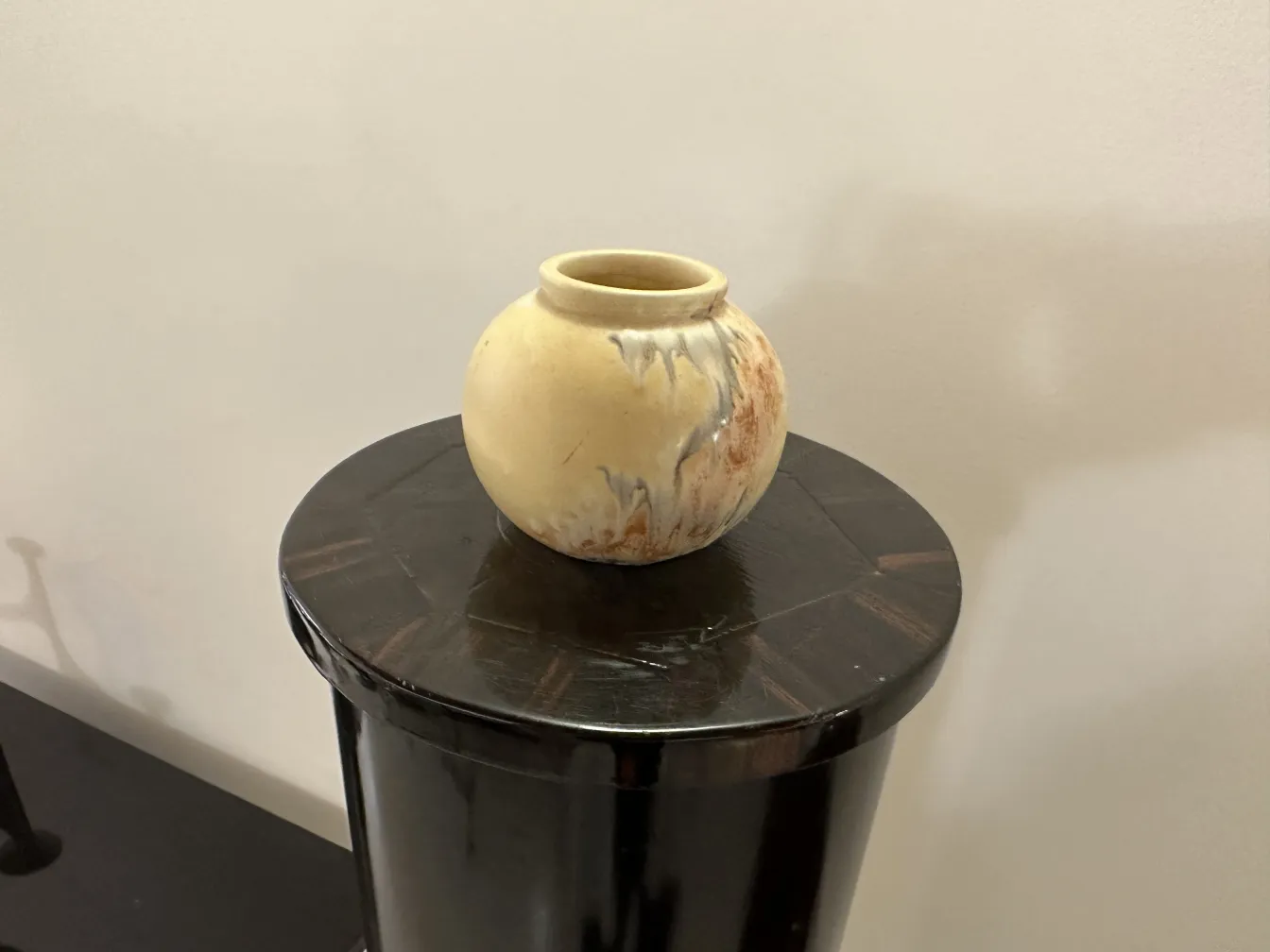 Vaso antigo cerâmico pintado em tons amarelos e marrons, descansando sobre uma superfície preta.