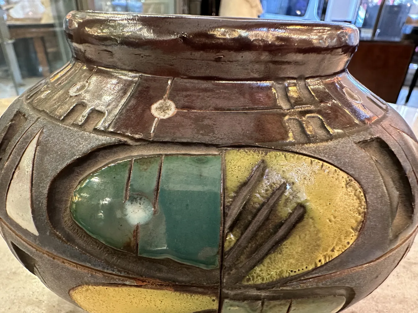 Antique ceramic vase with relief decorations, featuring terracotta and green tones on a neutral background.