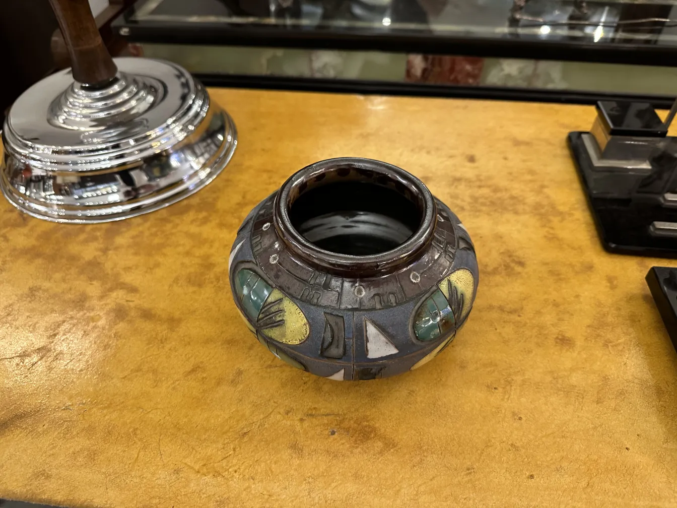 Vaso di ceramica antica con disegni colorati e forme geometriche, posato su una superficie marrone.