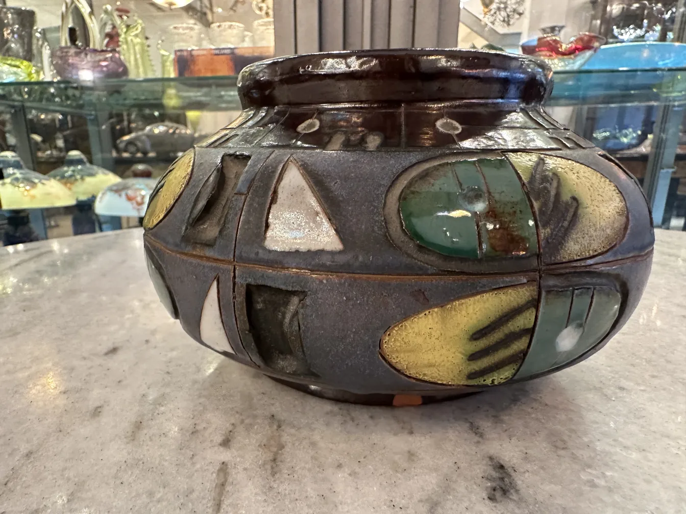 Antiker Keramikvase mit buntem Design, Regale im Hintergrund.